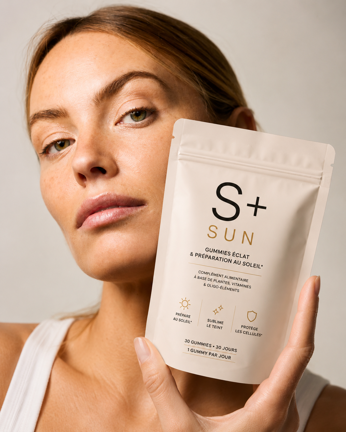 Woman with a golden glow holding a pouch of S+ SUN self-tanning gummies